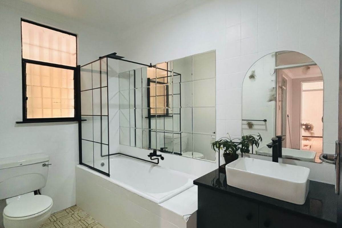 A modern-style bathroom featuring a bathtub with a black-framed screen, a vessel sink vanity, and a toilet, finished with patterned floor tiles.
