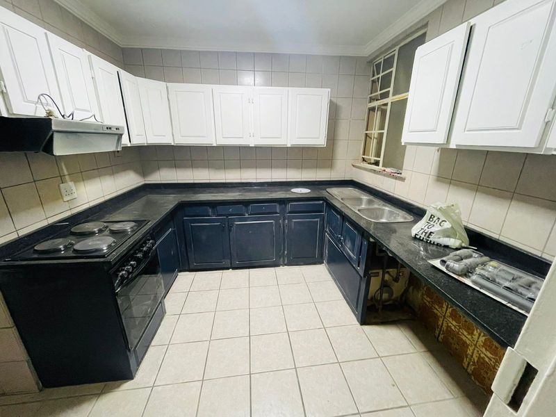 A functional U-shaped kitchen featuring dark lower cabinetry, white upper cabinets, stone countertops, and a built-in electric stove with an extractor fan.