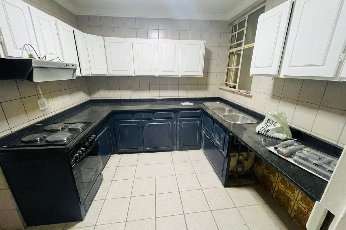 A functional U-shaped kitchen featuring dark lower cabinetry, white upper cabinets, stone countertops, and a built-in electric stove with an extractor fan.