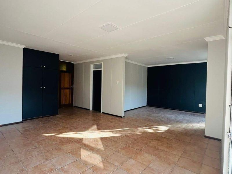 Spacious, empty living area featuring neutral tiled flooring, built-in storage cupboards, and contrasting dark accent walls.