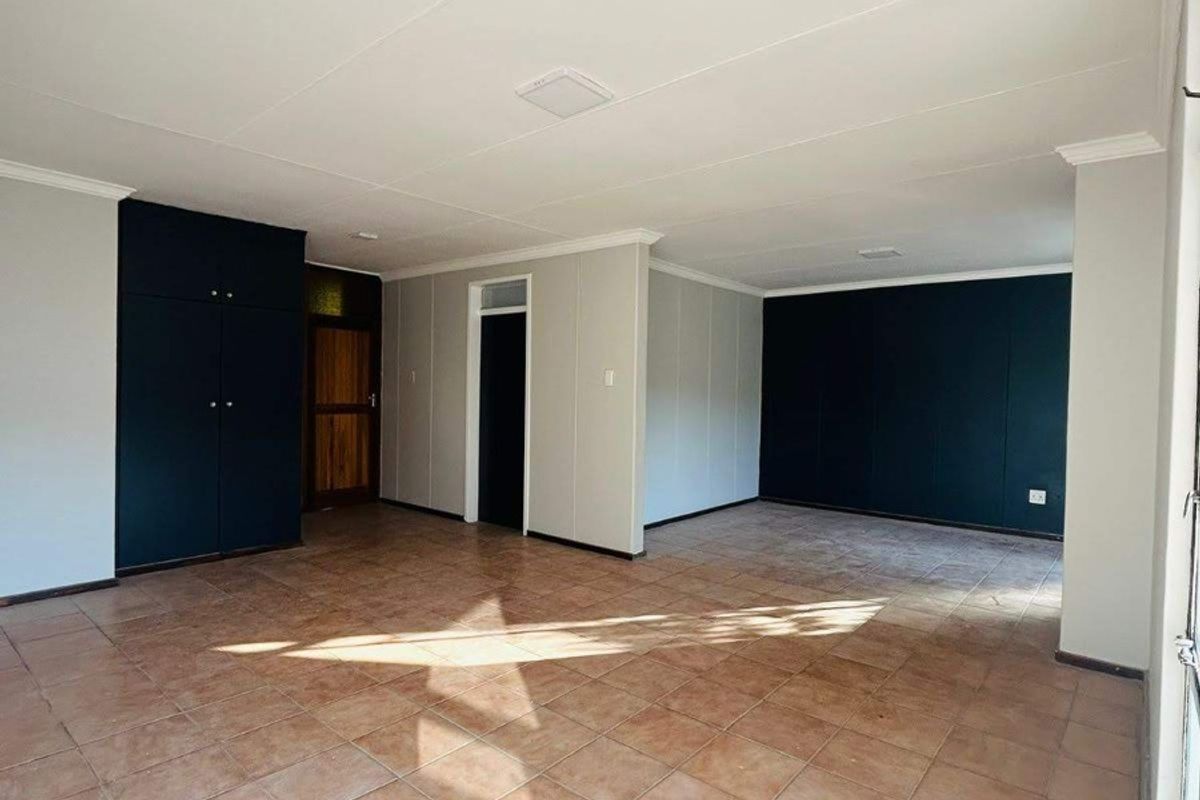 Spacious, empty living area featuring neutral tiled flooring, built-in storage cupboards, and contrasting dark accent walls.
