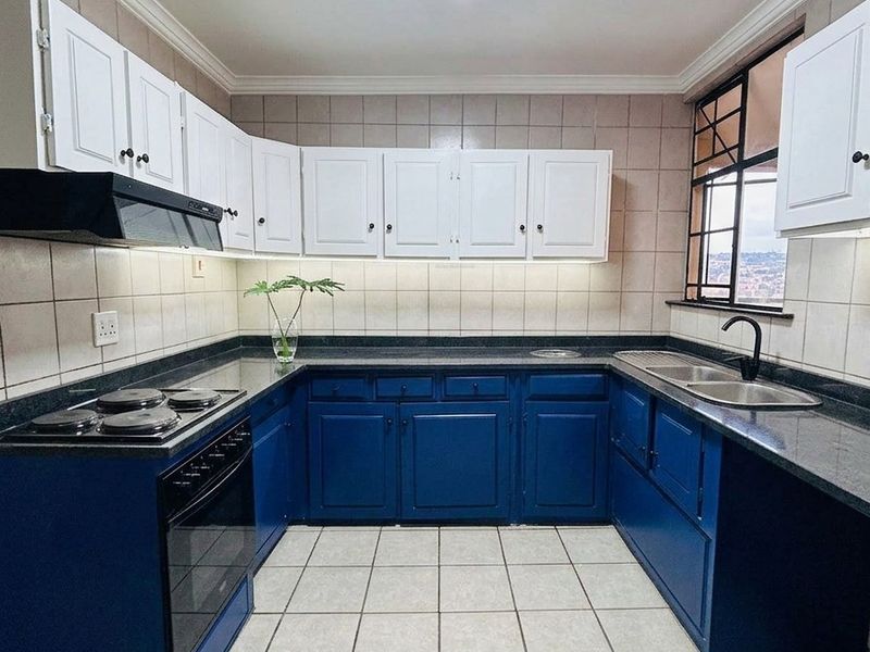 A well-maintained kitchen featuring blue lower cabinetry, white upper cabinets, granite countertops, and a built-in electric stove with an extractor fan.