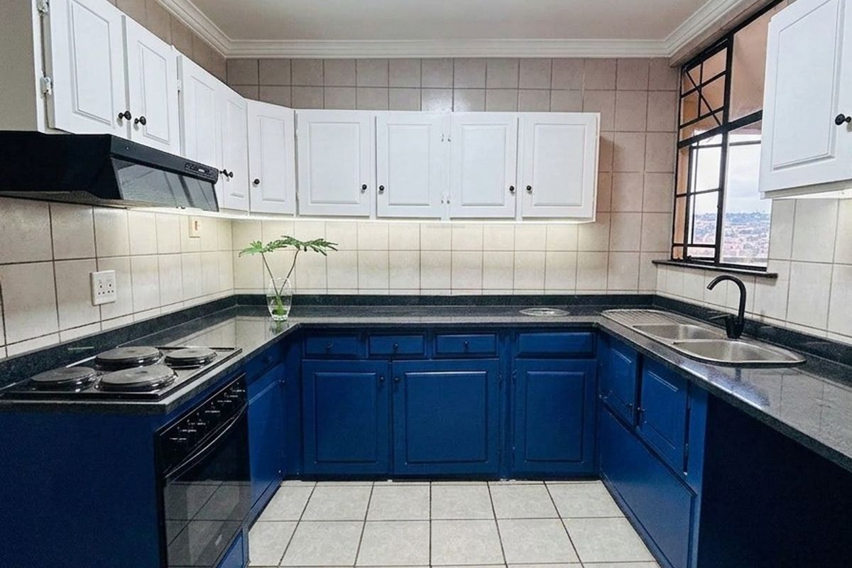 A well-maintained kitchen featuring blue lower cabinetry, white upper cabinets, granite countertops, and a built-in electric stove with an extractor fan.