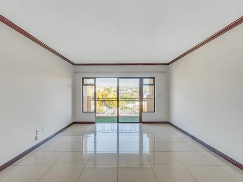 A bright, empty living room featuring polished tile flooring, crown molding, and a sliding glass door leading to a balcony with scenic views.