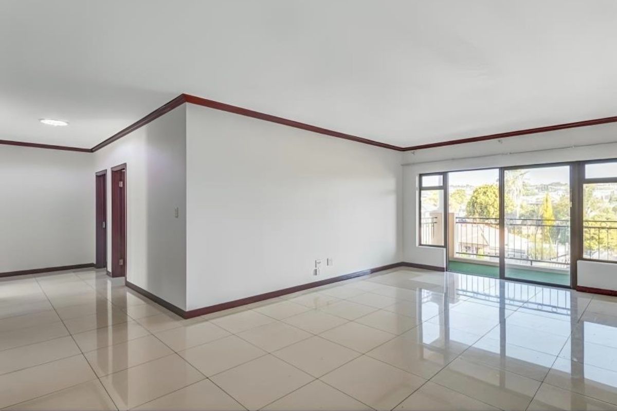 Spacious, light-filled living area featuring polished tile flooring, timber trim detailing, and direct access to a private balcony through sliding glass doors.