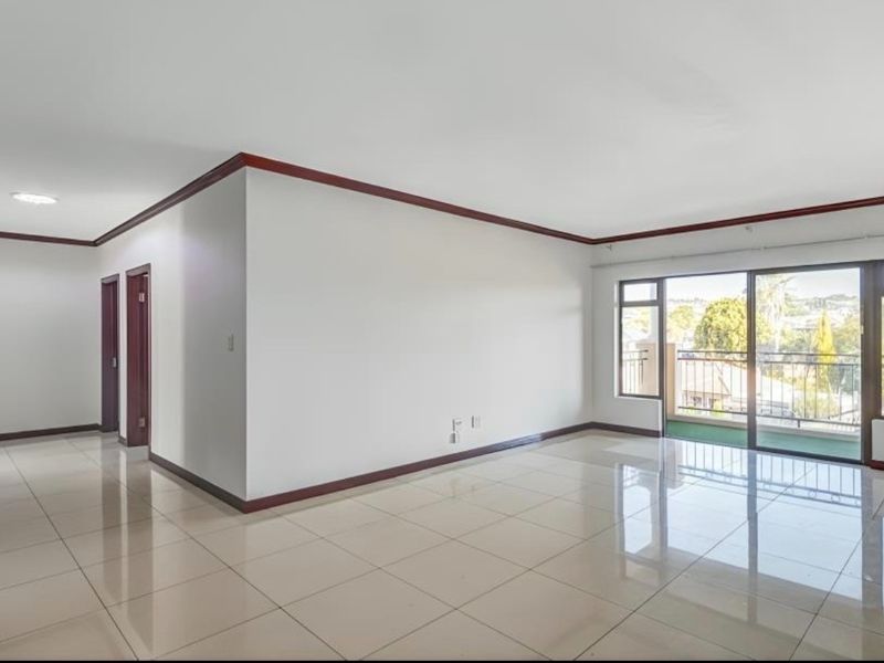 Spacious, light-filled living area featuring polished tile flooring, timber trim detailing, and direct access to a private balcony through sliding glass doors.