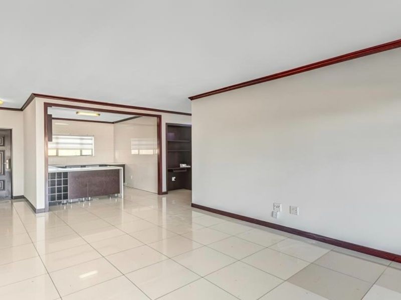 Spacious open-plan living area featuring tiled floors, built-in kitchen cabinetry with a wine rack, and a secure entrance door.
