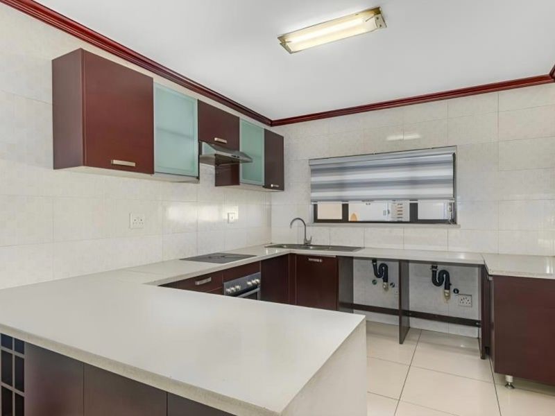 A functional kitchen featuring dark cabinetry, stone countertops, built-in appliances, and tiled finishes, currently awaiting final cabinet door installation under the sink.