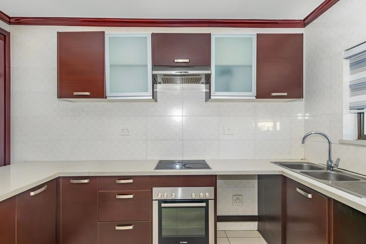 A clean, functional kitchen featuring dark wood cabinetry, stone countertops, built-in oven, electric cooktop, and a stainless steel sink with tiled backsplash.