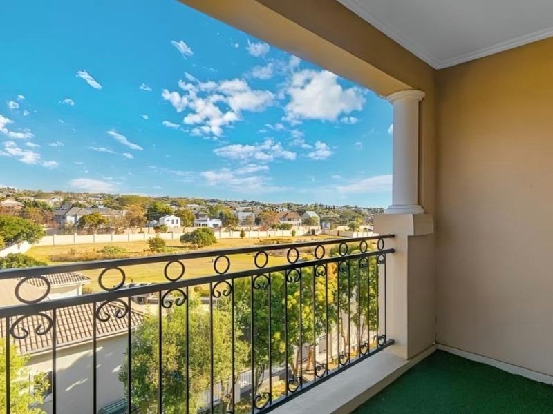 A covered balcony featuring a decorative wrought iron balustrade and a classic column, offering an elevated view over the surrounding residential area.