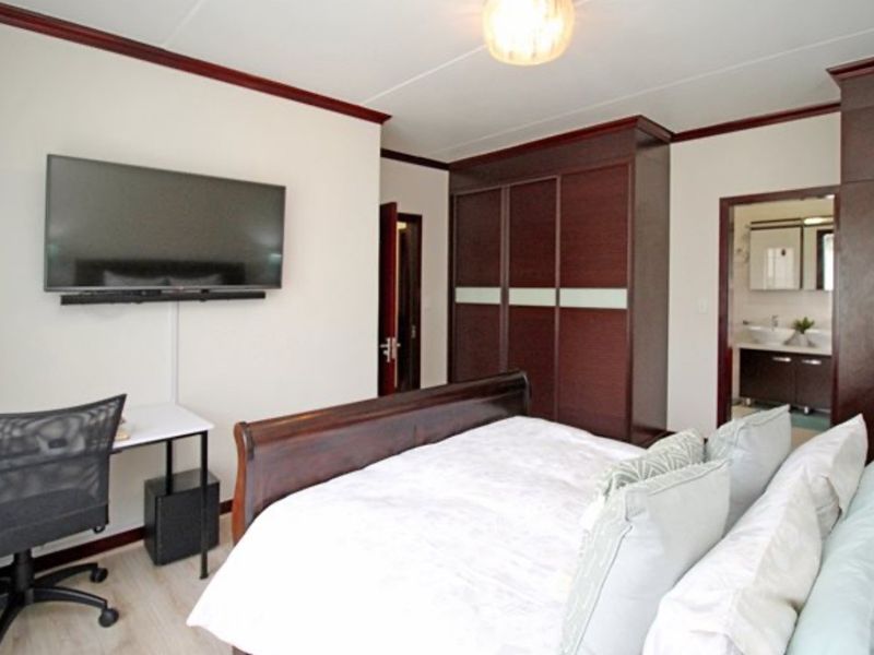 A well-maintained bedroom featuring built-in dark wood wardrobes, laminate flooring, and decorative coving, with an adjoining en-suite bathroom.