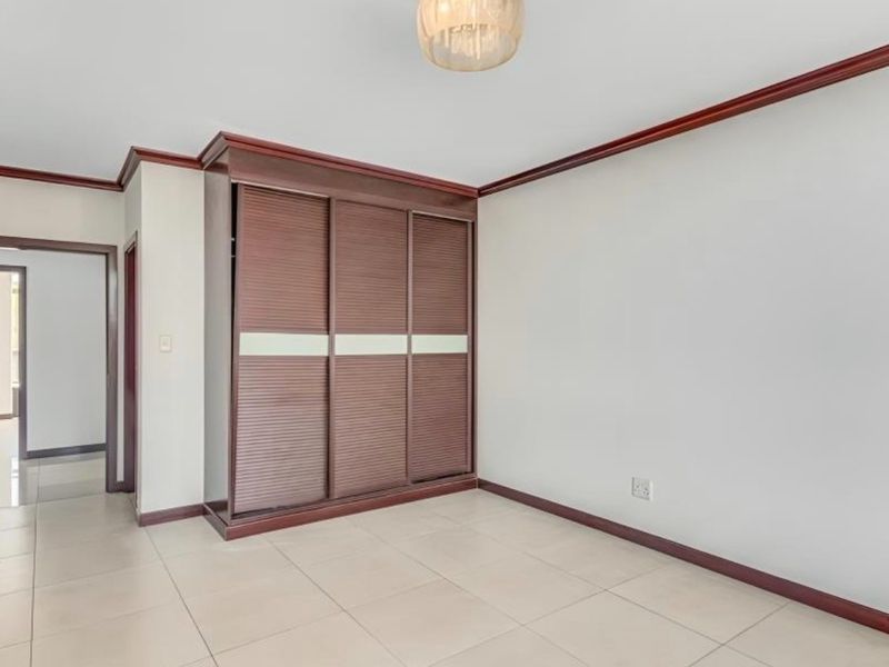 A bright, empty bedroom featuring neutral tiled flooring, dark wood crown molding, and a large built-in sliding door wardrobe.
