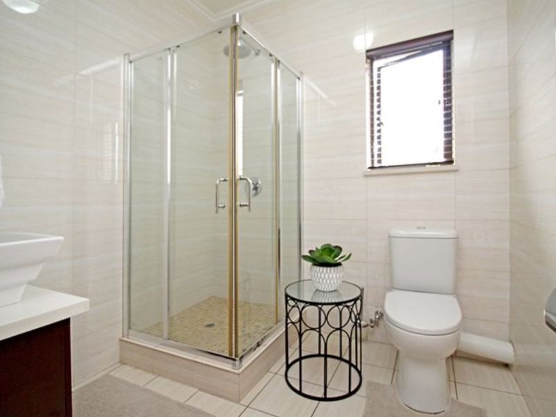 A clean and functional bathroom featuring a corner shower enclosure, ceramic wall and floor tiles, and a modern vanity basin.