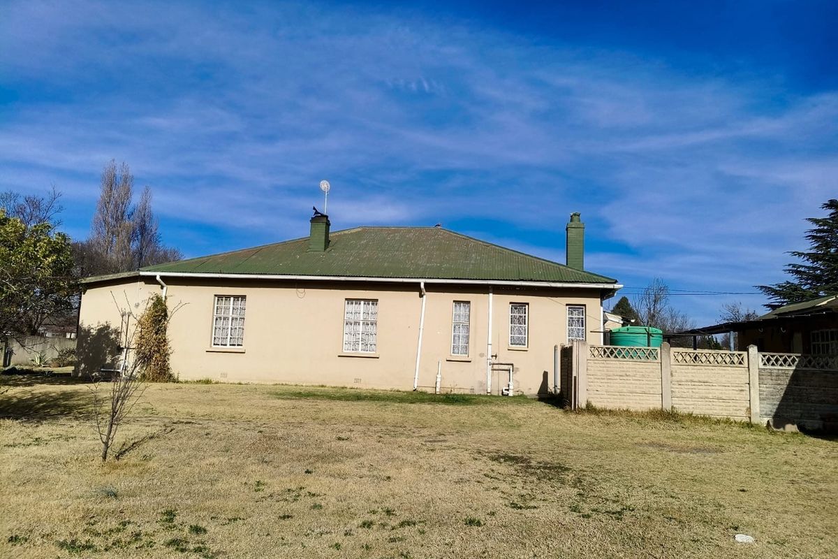 Rear view of the house featuring a corrugated metal roof, chimneys, and a large garden area with a precast concrete boundary wall.