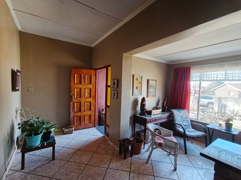 A living area featuring tiled flooring, a timber entrance door, and a large window with security bars, requiring cosmetic updates to improve its appeal.