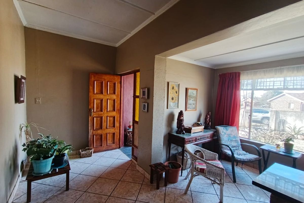 A living area featuring tiled flooring, a timber entrance door, and a large window with security bars, requiring cosmetic updates to improve its appeal.