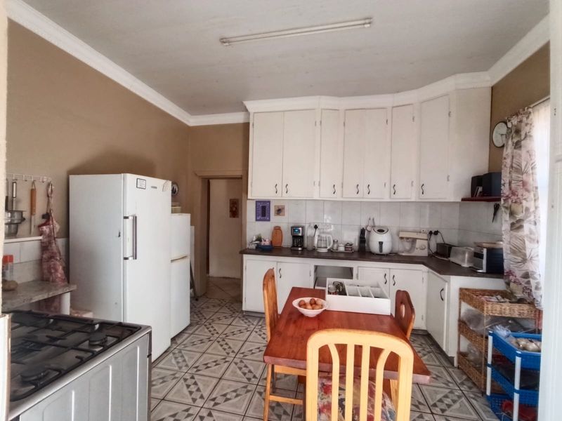A functional kitchen featuring white built-in cabinetry, a gas hob, tiled backsplash, and patterned floor tiles, offering a classic layout with potential for modernization.