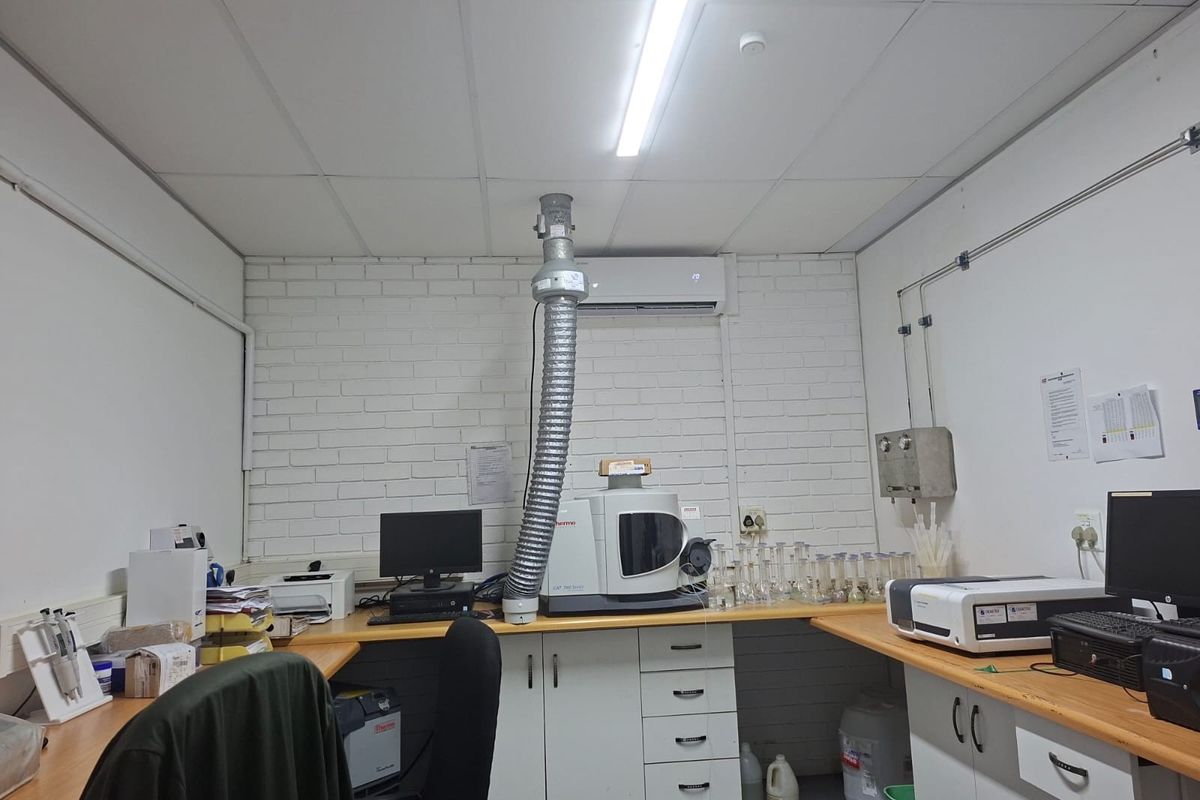 A functional commercial laboratory space featuring built-in cabinetry, specialized fume extraction ducting, and integrated split-system air conditioning.
