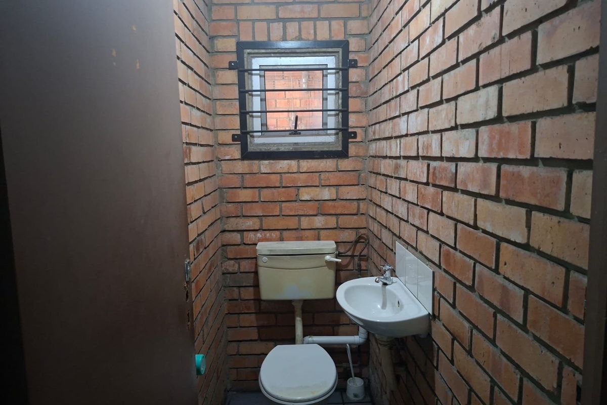 A compact bathroom featuring exposed brick walls, a wall-mounted basin, and a standard toilet with a window protected by security bars.