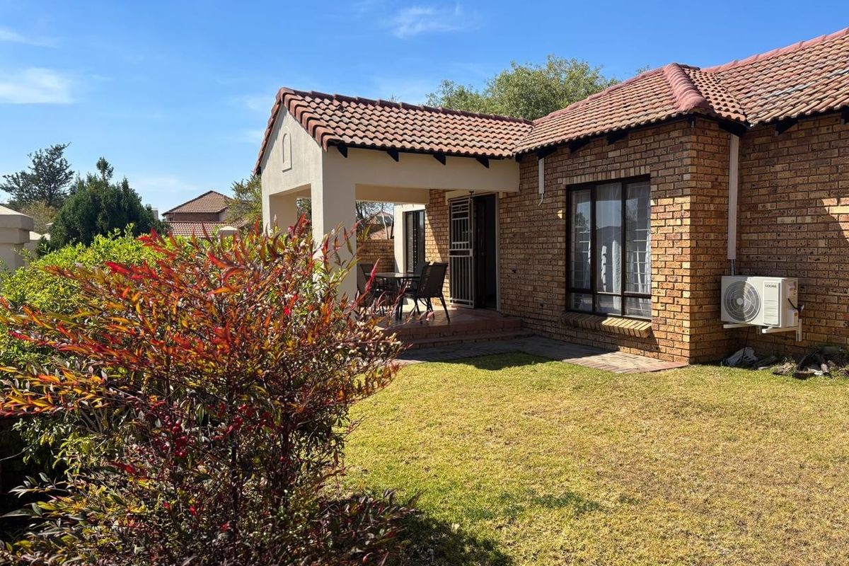 A rear view of the house featuring a brick facade, a covered patio area, and a well-maintained garden lawn.
