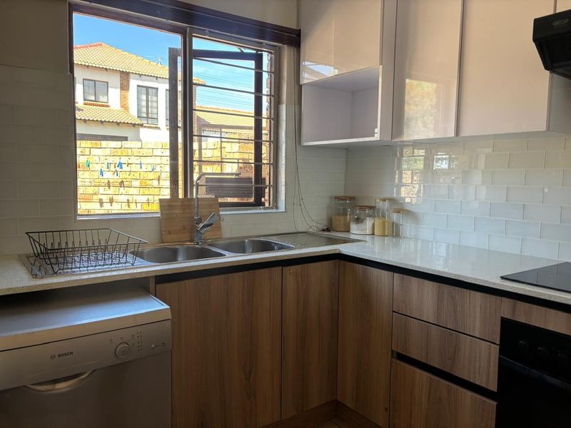 Modern kitchen featuring wood-finish cabinetry, white subway tile backsplash, quartz countertops, and integrated appliances including an oven and hob.
