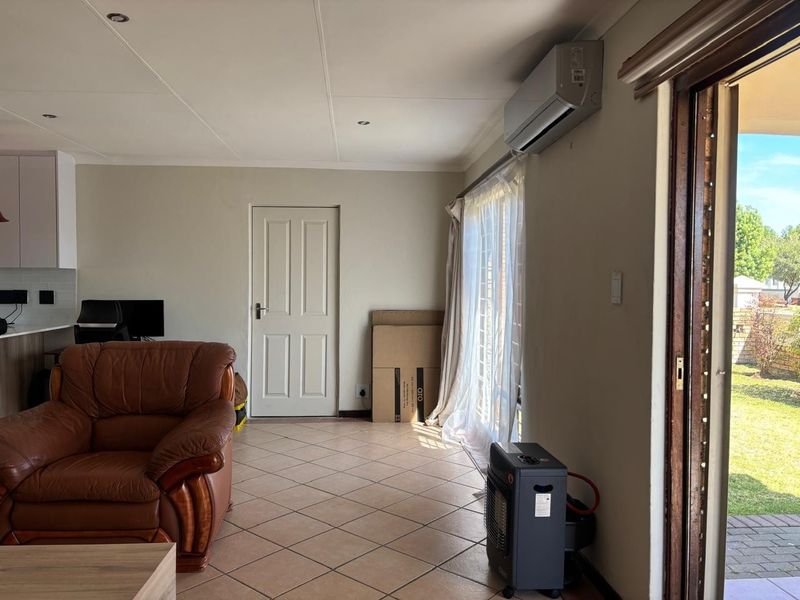 Open plan living area featuring tiled flooring, a wall-mounted air conditioning unit, and direct access to the garden through a sliding glass door.