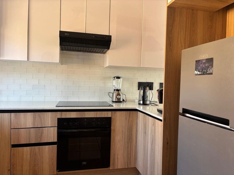 Modern kitchen featuring wood-grain cabinetry, white subway tile backsplash, stone countertops, and integrated appliances including an electric hob and oven.