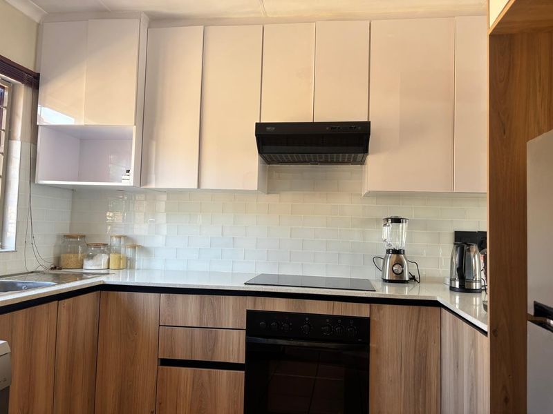 Modern kitchen featuring sleek two-tone cabinetry, subway tile backsplash, stone countertops, and integrated appliances including an electric hob and oven.