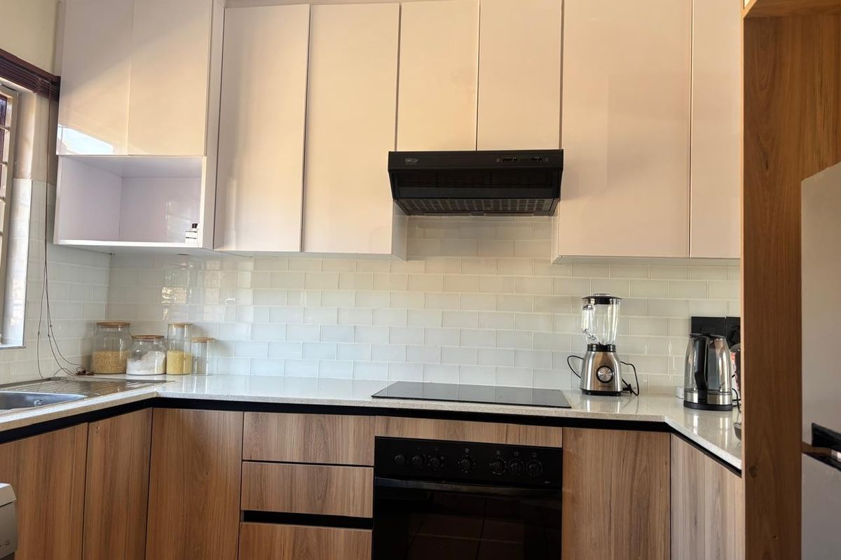Modern kitchen featuring sleek two-tone cabinetry, subway tile backsplash, stone countertops, and integrated appliances including an electric hob and oven.