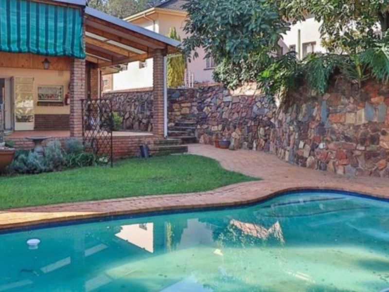 Outdoor pool area featuring a swimming pool, brick retaining wall, and a covered patio space with brick paving.