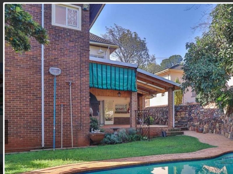 Rear exterior view featuring a swimming pool, brick facade, and a covered patio area with a stone retaining wall.