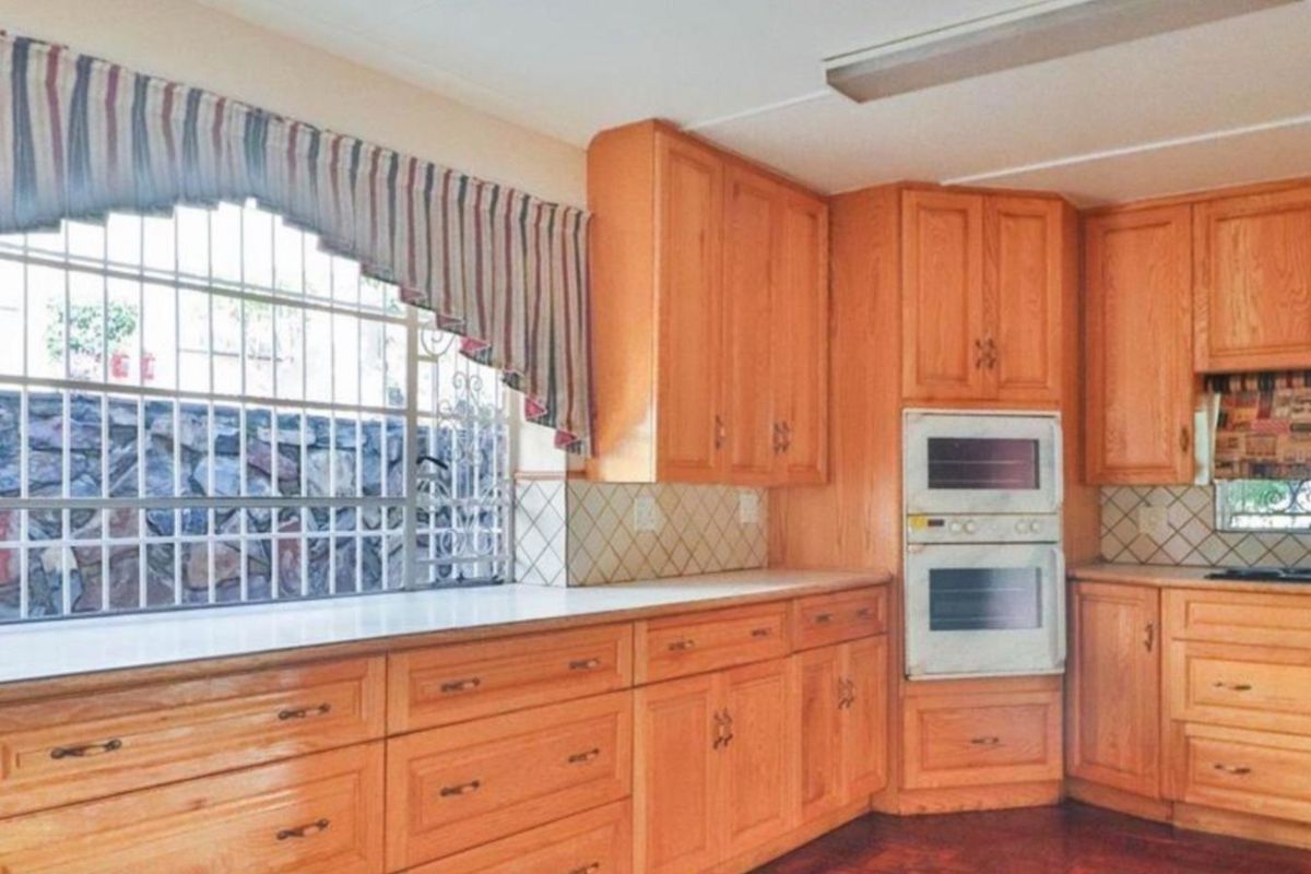 A functional kitchen featuring extensive wooden cabinetry, a built-in double oven, integrated hob, and tiled backsplash with security bars on the window.