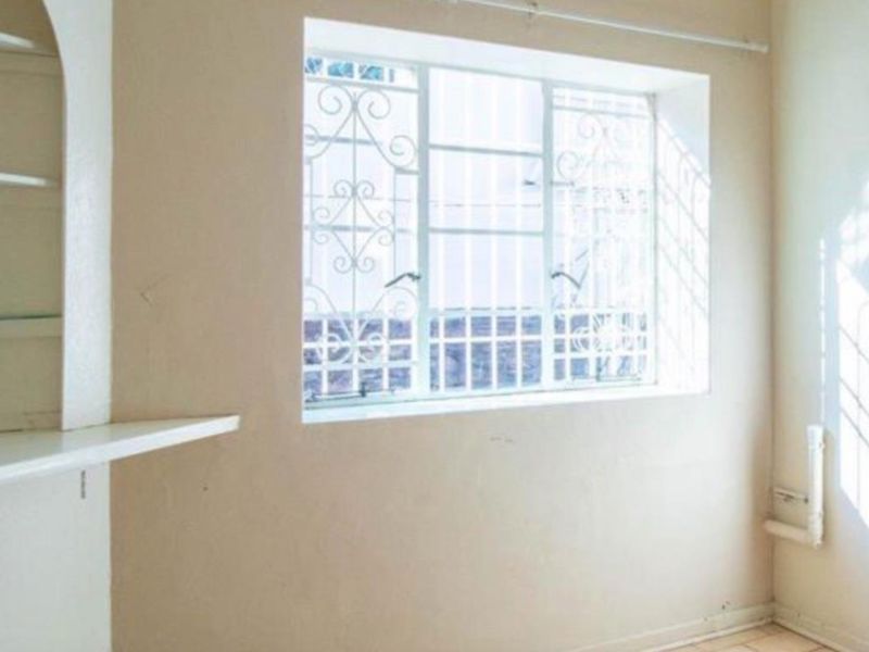 A vacant utility or storage space featuring built-in shelving, tiled flooring, and a window fitted with security bars.