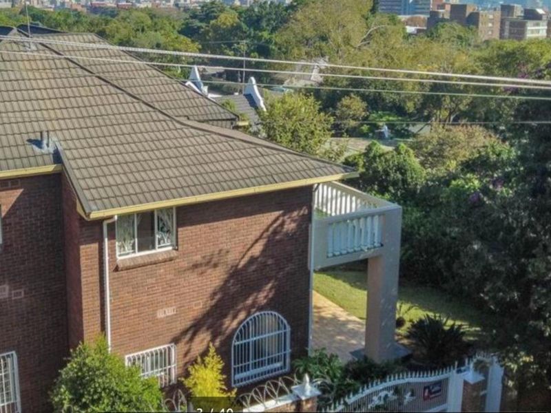 Elevated view of the rear exterior featuring a brick facade, tiled roof, and a balcony overlooking the surrounding garden and neighborhood.