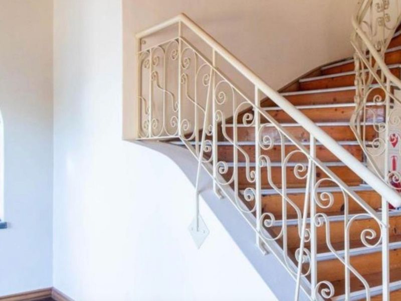 A bright hallway featuring a timber staircase with a decorative wrought iron balustrade and an arched window.