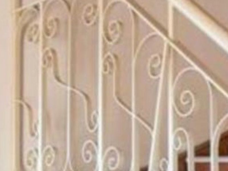 A bright hallway featuring a timber staircase with a decorative wrought iron balustrade and an arched window.