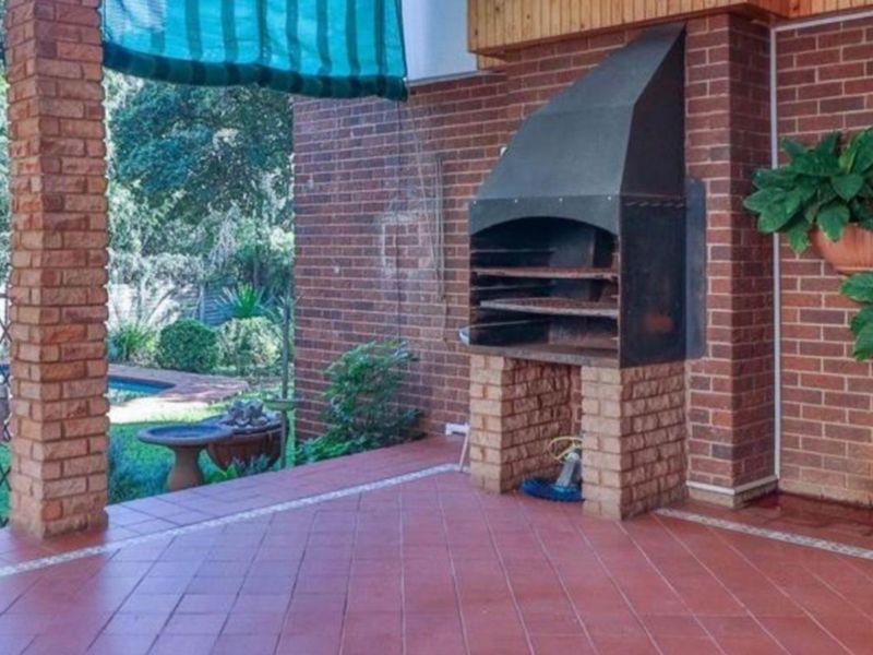 Covered patio area featuring a built-in brick braai, tiled flooring, and direct access to the garden and pool area.