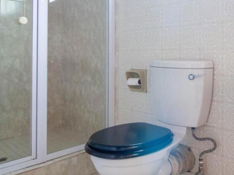 A functional bathroom featuring a shower enclosure, standard toilet, and wall-mounted washbasin with dated tiling throughout.