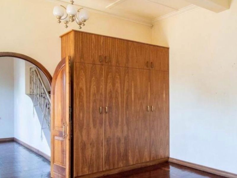 A spacious bedroom featuring polished hardwood flooring, a large built-in wooden wardrobe, and an elegant arched doorway leading to an adjacent area.