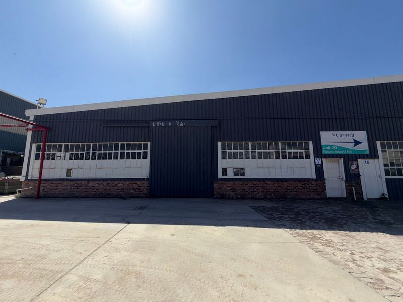 Front elevation of an industrial warehouse unit featuring corrugated metal cladding, large sliding access door, and multi-pane industrial windows with a concrete forecourt.