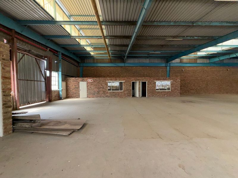 Spacious industrial warehouse unit featuring exposed steel roof trusses, concrete flooring, and brick wall construction with integrated office or utility access points.