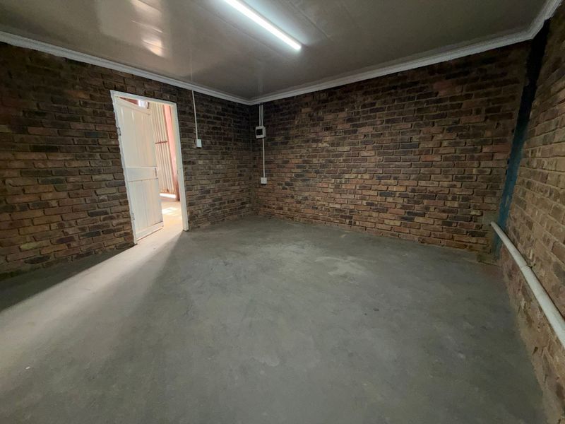 A functional utility space featuring exposed brick walls, concrete flooring, and overhead fluorescent lighting, suitable for storage or workshop use.