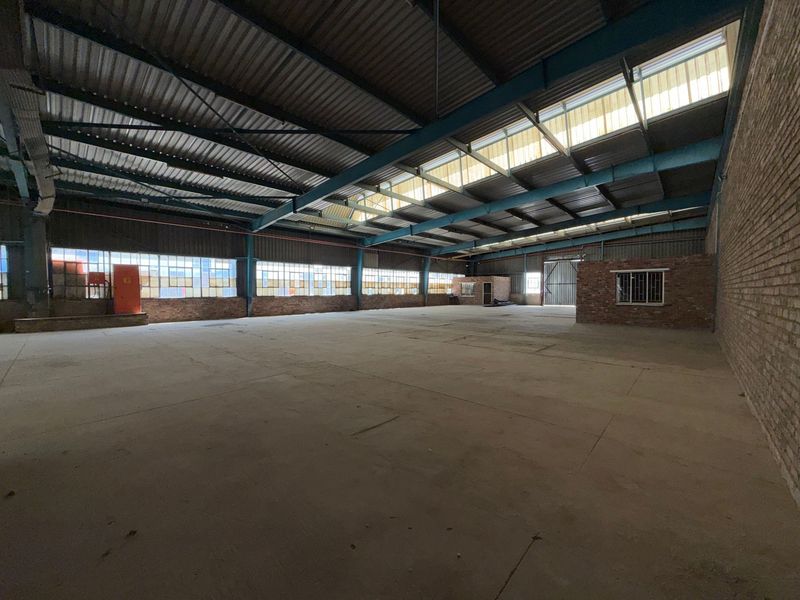 Spacious industrial warehouse featuring high ceilings with exposed steel trusses, abundant natural light from skylights, and durable concrete flooring.