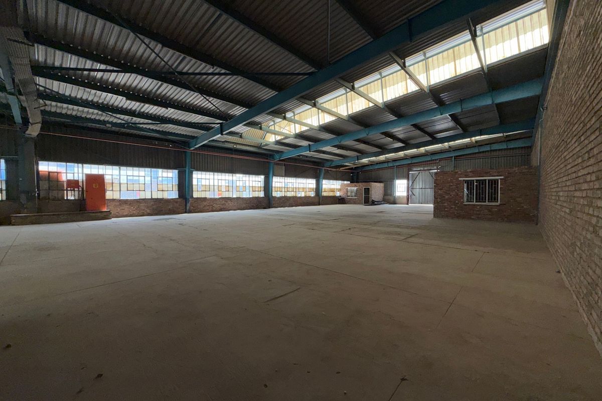 Spacious industrial warehouse featuring high ceilings with exposed steel trusses, abundant natural light from skylights, and durable concrete flooring.