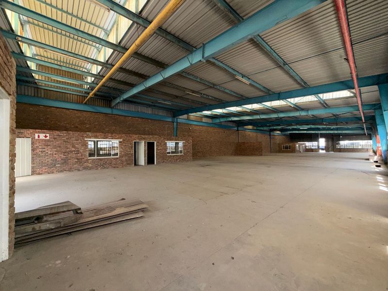 Spacious industrial warehouse featuring exposed steel trusses, high ceilings with skylights, durable concrete flooring, and exposed brick walls, offering a versatile open-plan workspace.