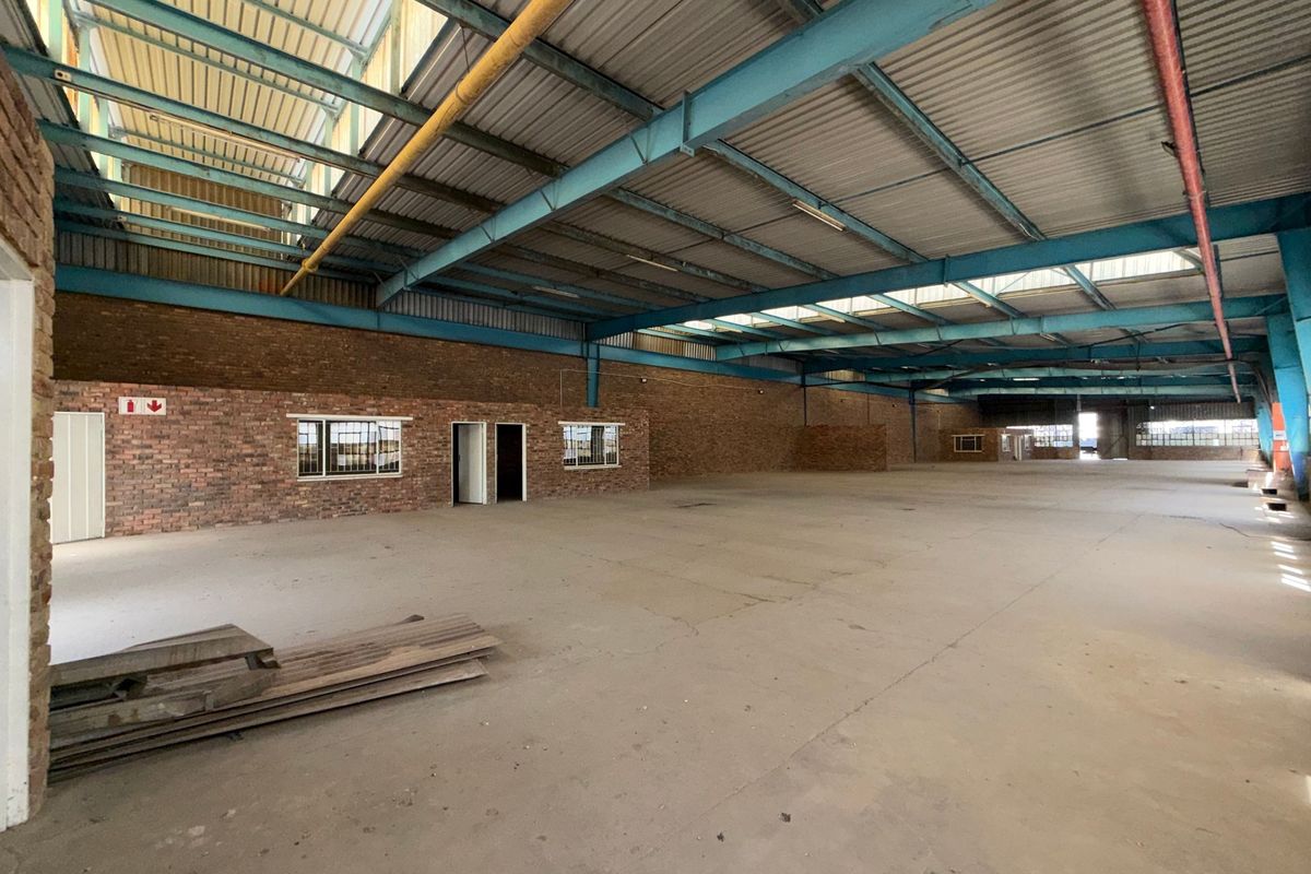 Spacious industrial warehouse featuring exposed steel trusses, high ceilings with skylights, durable concrete flooring, and exposed brick walls, offering a versatile open-plan workspace.