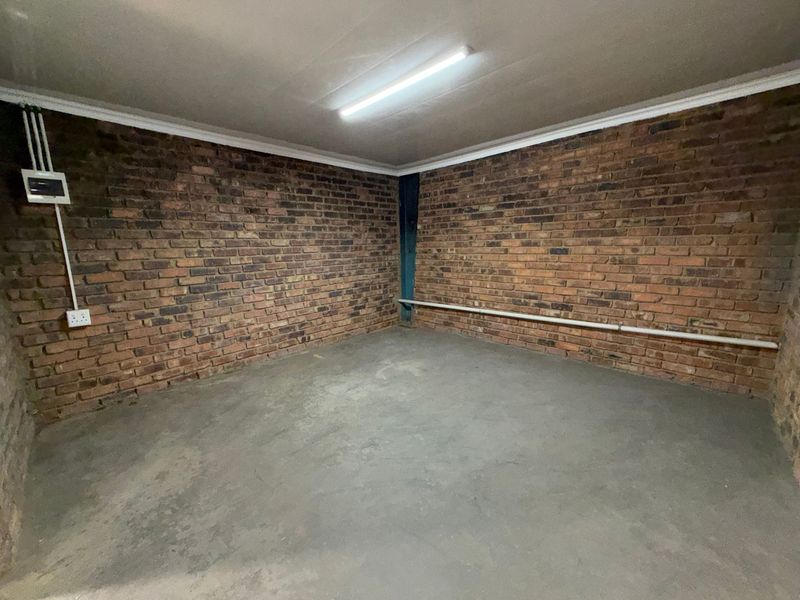 An empty utility space featuring exposed brick walls, concrete flooring, and functional overhead lighting, suitable for storage or workshop use.
