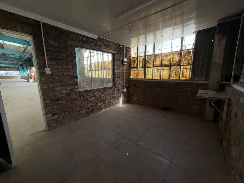 An empty industrial utility space featuring exposed brick walls, tiled flooring, and large steel-framed windows providing natural light.