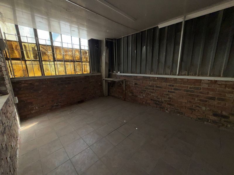 An empty industrial utility space featuring exposed brick walls, tiled flooring, and a wall-mounted sink, suitable for storage or workshop use.