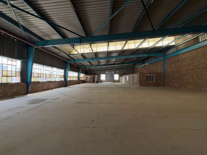Spacious industrial warehouse featuring high ceilings with exposed steel trusses, concrete flooring, and large steel-framed windows providing ample natural light.